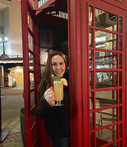 Woman in an old fashioned phone booth holds a hot toddy from Le Bar Marche.
